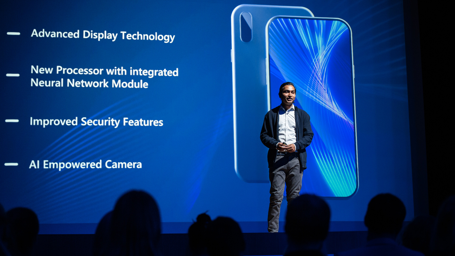 Live Event with New Products Reveal: Keynote Speaker Presents Smartphone Device to Audience. Movie Theater Screen Shows Mock-up Touch Screen Mobile Phone with High End Features and Top Highlights